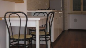 A small kitchen with a dining table and chairs, a refrigerator, and a window with blinds. - GREEN RELAX II THE GREEN OF THE HILL (Torino)