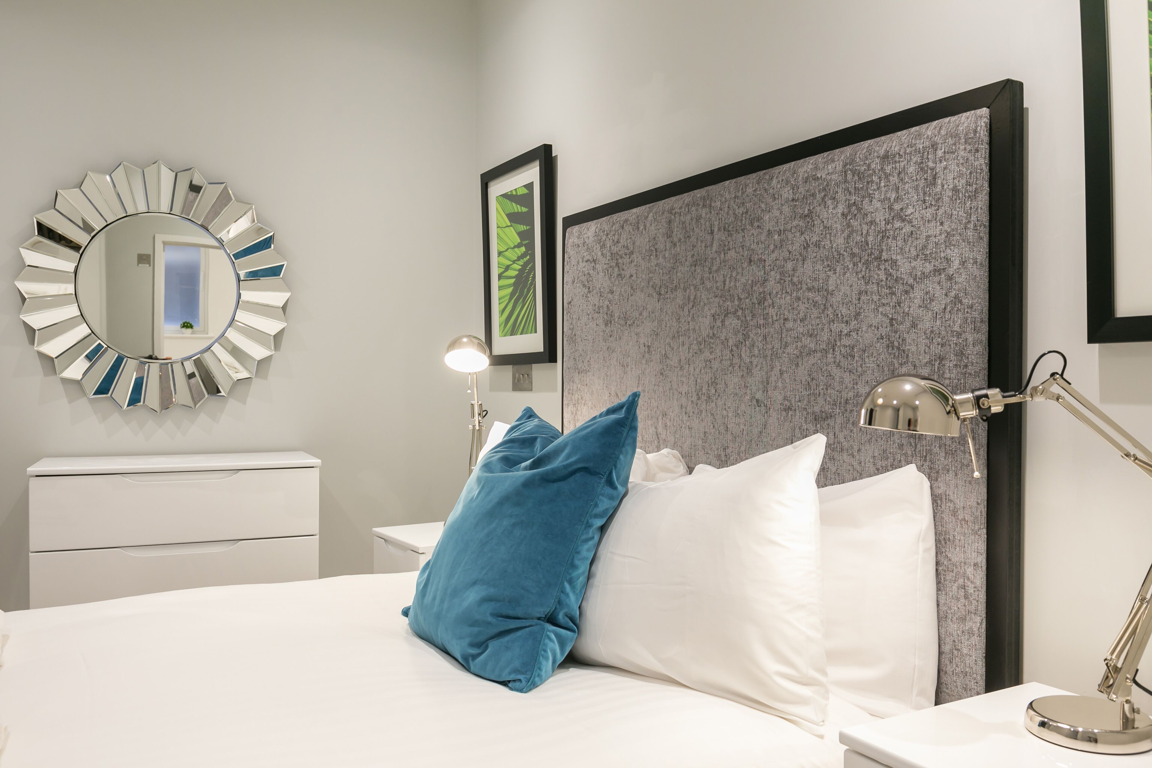 Een moderne hotelkamer met een groot bed, een ronde spiegel, een bedlampje en een ingelijste foto aan de muur.