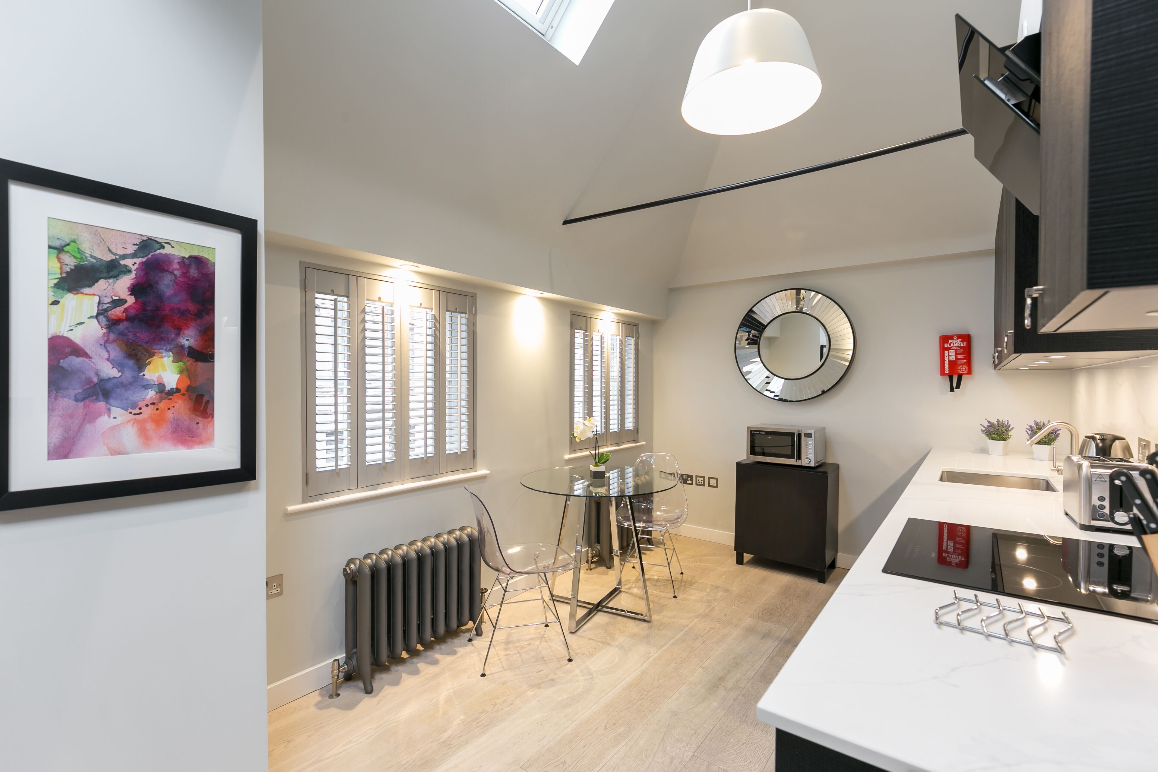 A modern kitchen with a central island, a dining area with a glass table, and a large mirror on the wall.