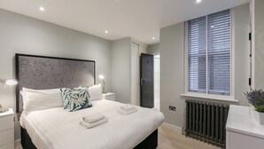Et moderne soveværelse med en stor seng, sengeborde med lamper, en radiator og et vindue med persienner.