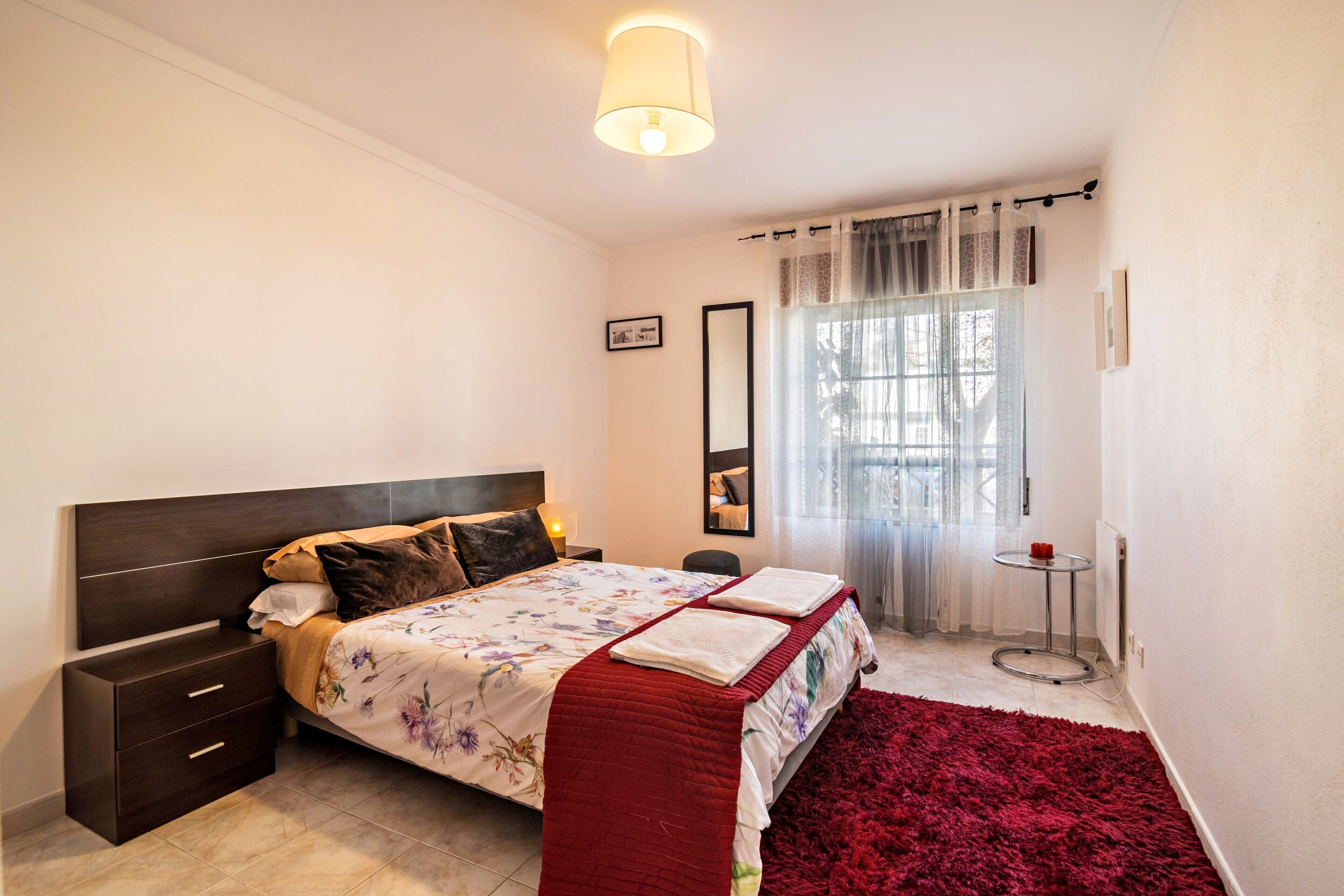 A bedroom with a bed, nightstand, bedside table, and a window with curtains.