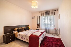 Une chambre à coucher comprenant un lit, une table de chevet, une commode et une fenêtre avec des rideaux.