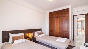 A hotel room with two beds, wooden wardrobe, and a nightstand with a lamp. - Cosy Vacation Home “Casa da Praia” close to the Beach with Wi-Fi (Tavira - Santa Luzia)