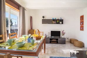Un coin repas avec une table mise pour le petit-déjeuner, un téléviseur et une étagère ornée d’objets décoratifs.