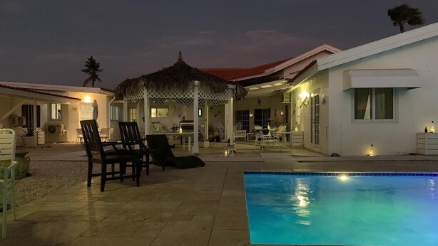 Zona de piscina con sillones de descanso y un área de estar cubierta.