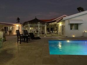 Zona de piscina con sillones de descanso y un área de estar cubierta.
