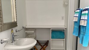 Un baño con un lavamanos blanco, un espejo, un perchero con toallas a rayas y una repisa con una toalla azul.
