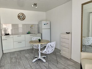 A compact kitchen with white cabinets, a round table, and a white chair.