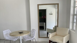 Una habitación con una mesa redonda, dos sillas blancas, un sillón beige y un espejo grande en la pared.