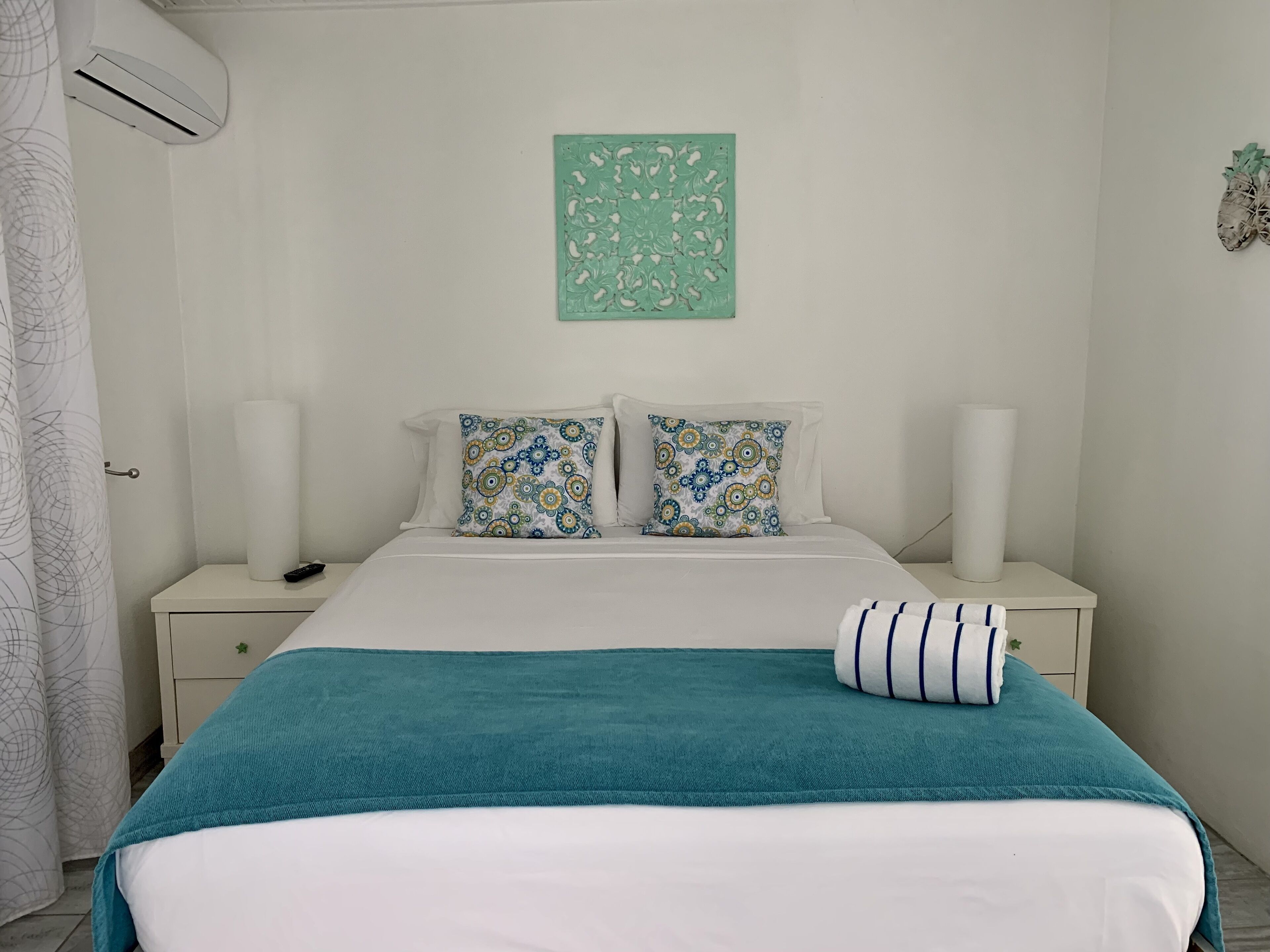 Ein ordentlich bezogenes Bett mit einer türkisblauen Decke, zwei gemusterten Kissen und einem weißen Kopfteil.