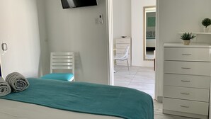 Un dormitorio con cama, televisor montado en la pared, escritorio con silla y cómoda.