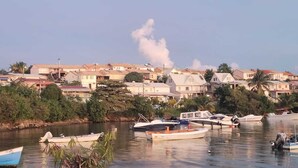 Un pueblo costero con casas a lo largo del frente marítimo, barcos amarrados en el agua y un cielo despejado.