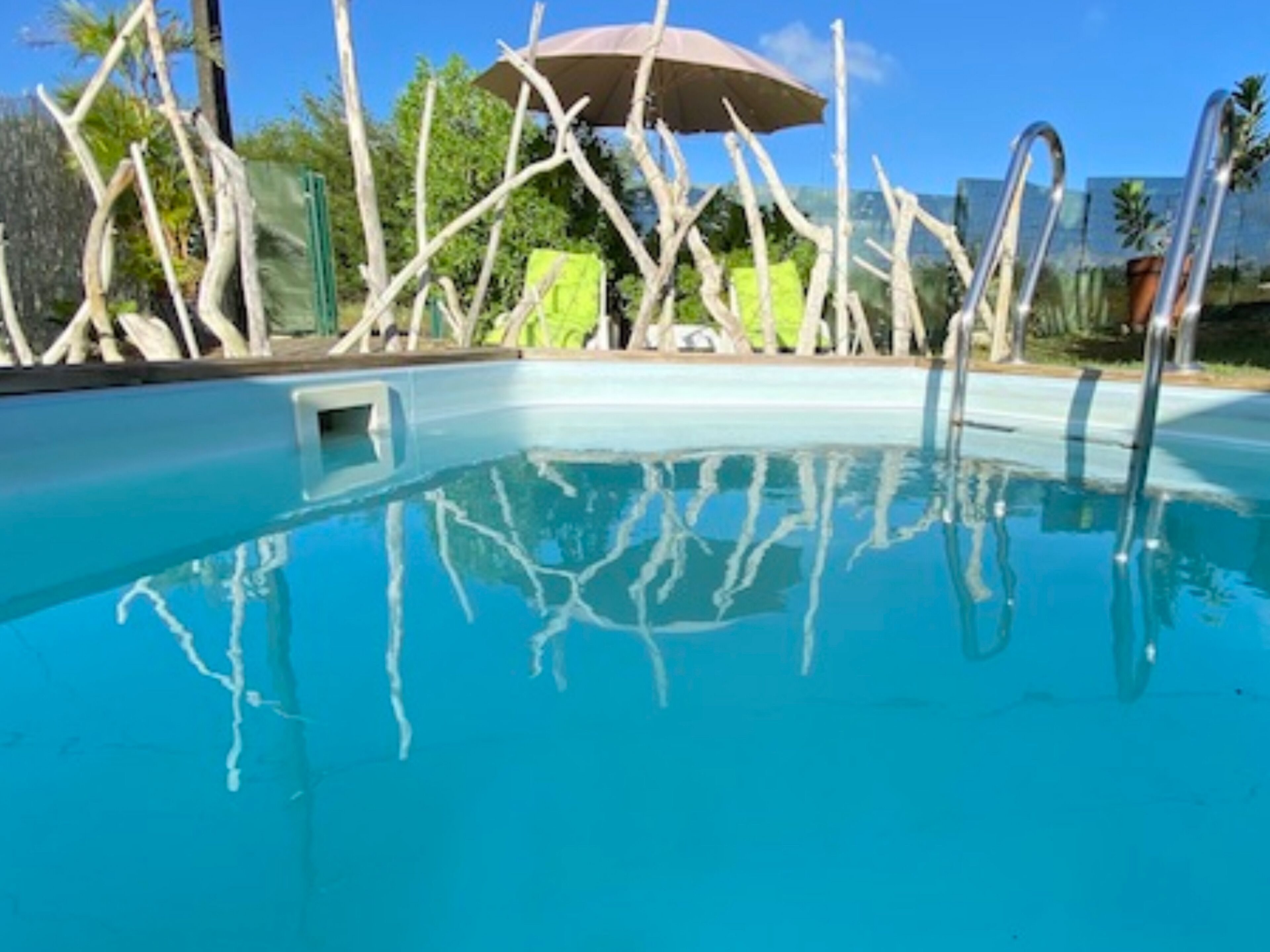 Ein Schwimmbecken mit klarem, blauem Wasser, umgeben von einer Holzterrasse und einem grünen Sonnenschirm.