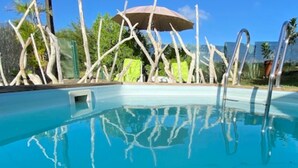 Una piscina con agua azul cristalina, rodeada por una terraza de madera y un paraguas verde.