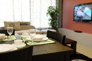 A dining table set with plates, glasses, and cutlery, a sofa in the background, and a TV mounted on the wall. - Two bed Furnished Apartment in Amman (Amman)