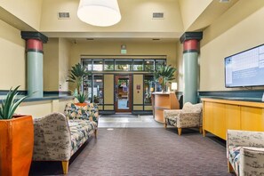 A lobby with a reception desk, patterned sofas, potted plants, and a large screen. - Corner Unit in the middle of it all - 99 Walkscore! (Seattle)