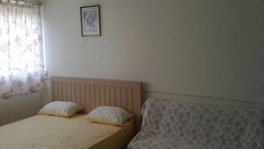 Un dormitorio con cama, cabecera, sofá, ventana con cortinas e imagen enmarcada en la pared.