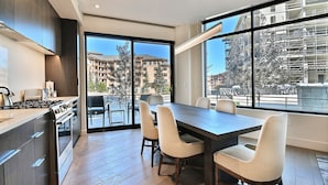 Une cuisine moderne dotée d’une grande table à manger et de chaises, d’un four encastré et offrant une vue sur la ville grâce à de grandes fenêtres.