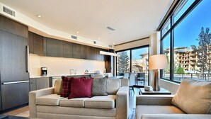 Un salon moderne avec un canapé et un fauteuil, une table basse et une vue sur un balcon avec un immeuble en arrière-plan.