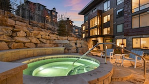 A heated outdoor pool with stone steps and lounge chairs, surrounded by a stone wall and modern buildings. - Mountain 1BR in Canyons Village-Ski in/ski out by RedAwning (Park City)