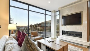 A modern living room with a large window, a fireplace, a sofa, and a coffee table. - Mountain 1BR in Canyons Village-Ski in/ski out by RedAwning (Park City)