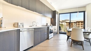 A modern kitchen with a large island, built-in appliances, and a dining area with a view of the city. - Luxury 2 BR in Canyons Village - Walk to Slopes by RedAwning (Park City)