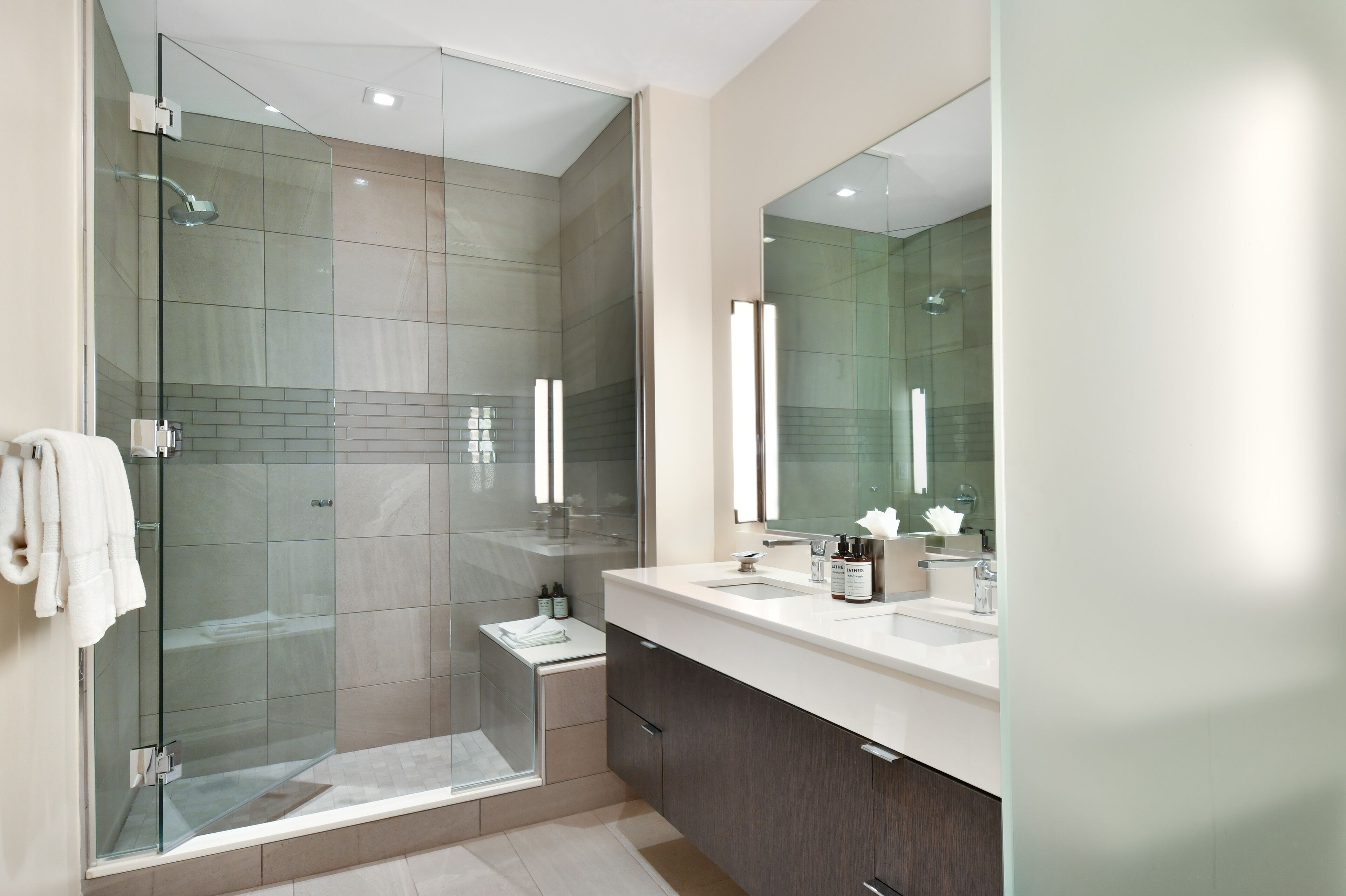 A modern bathroom with a glass-enclosed shower, a large mirror, and a white sink.