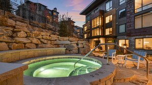 A heated outdoor pool with stone steps and lounge chairs, surrounded by a stone wall and modern buildings. - New 1 BR Residence in Canyons Village- Ski in/out by RedAwning (Park City)