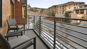 A balcony with wicker furniture, a view of a multi-story building, and a road with sparse vegetation. - Ski in/out Modern 2BR Residence in Canyons Village by RedAwning (Park City)