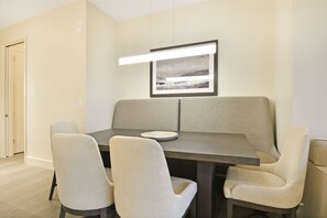 Un coin repas moderne avec une table en bois foncé, quatre chaises beiges à revêtement rembourré et un tableau encadré au-dessus de la table.