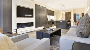 A modern living room with a fireplace, a kitchen area, and a seating area with sofas and a coffee table. - Ski in/out Modern 2BR Residence in Canyons Village by RedAwning (Park City)