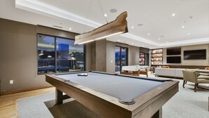 A pool table in a modern living room with a large window, a flat-screen TV, and a cozy seating area. - Ski in/out Modern 2BR Residence in Canyons Village by RedAwning (Park City)