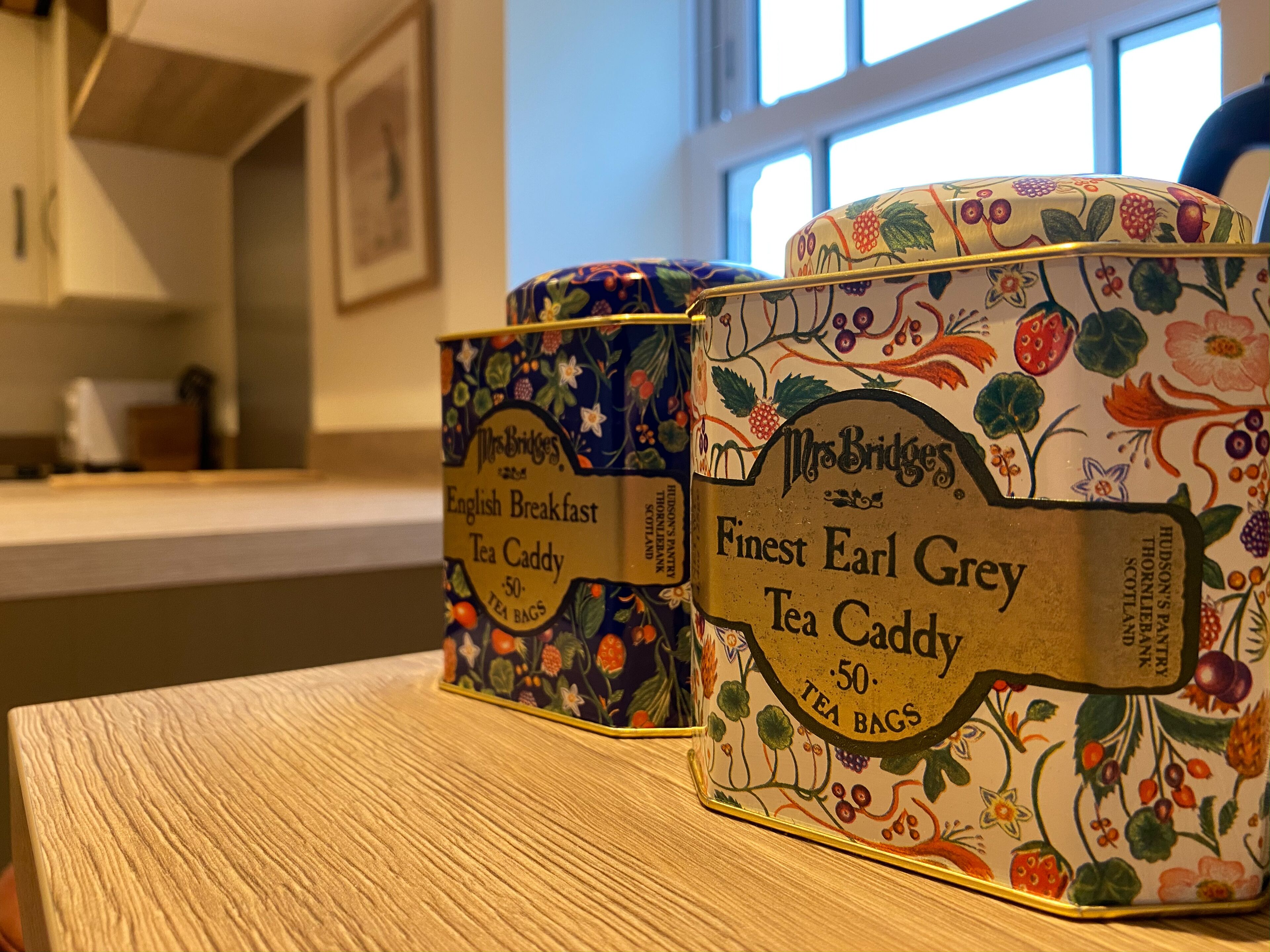 Tre contenitori per tè su un tavolo di legno, decorati con motivi floreali ed etichette che indicano tè Earl Grey.