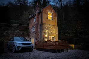 A stone house with a wooden bench in front, a car parked nearby, and a stone wall in the background. - Robin Hood Tower (Matlock)