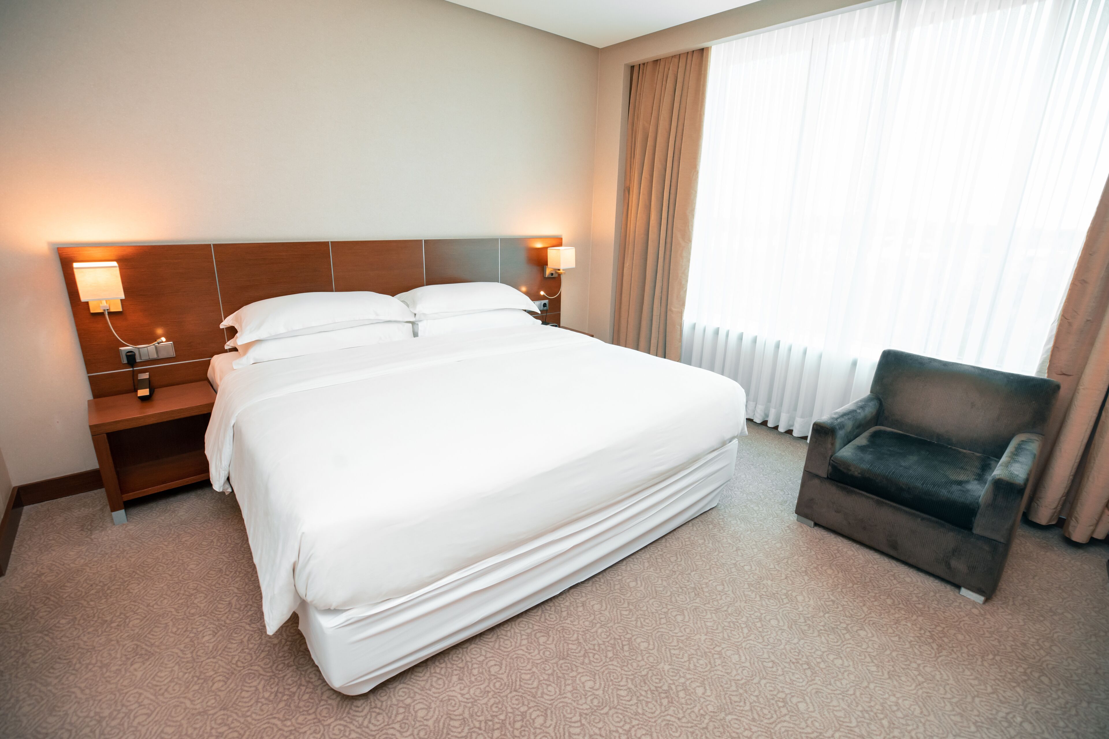 A hotel room with a large bed, two bedside tables, a chair, and a window with curtains.