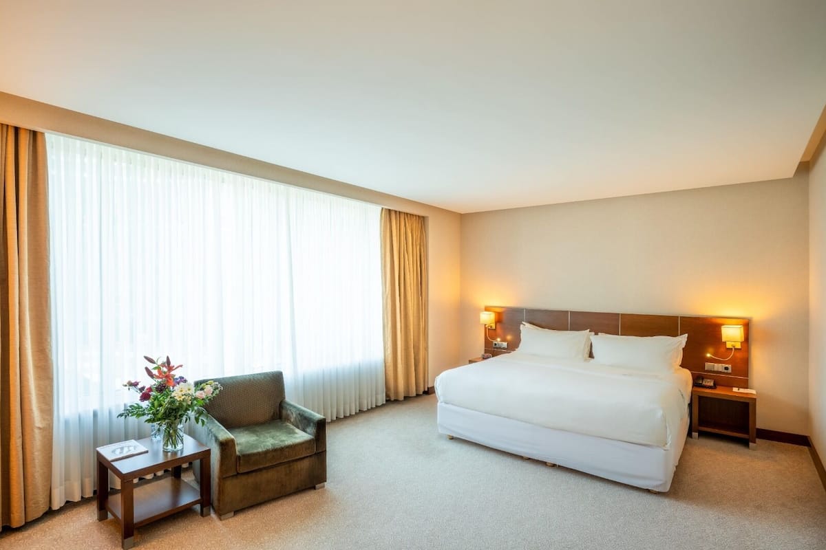 A hotel room with a large bed, a chair, a small table with a vase of flowers, and two bedside lamps.