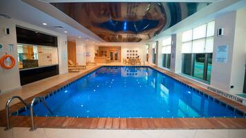 Una piscina interior con cubierta de madera, un flotador salvavidas y un cartel que indica profundidad sin permitido para buceo.