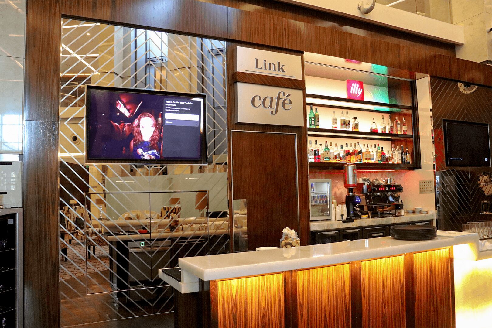 Zona de bar con una pantalla de televisión, un letrero que dice 'Link Café' y una variedad de botellas de licor en estantes.
