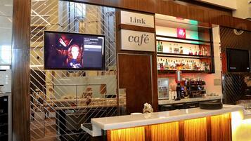 Zona de bar con una pantalla de televisión, un letrero que dice 'Link Café' y una variedad de botellas de licor en estantes.