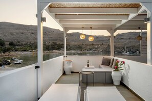 Un balcon donnant sur un plan d’eau et des bateaux, un pot blanc rempli de fleurs et une bouteille de vin posée sur une petite table.