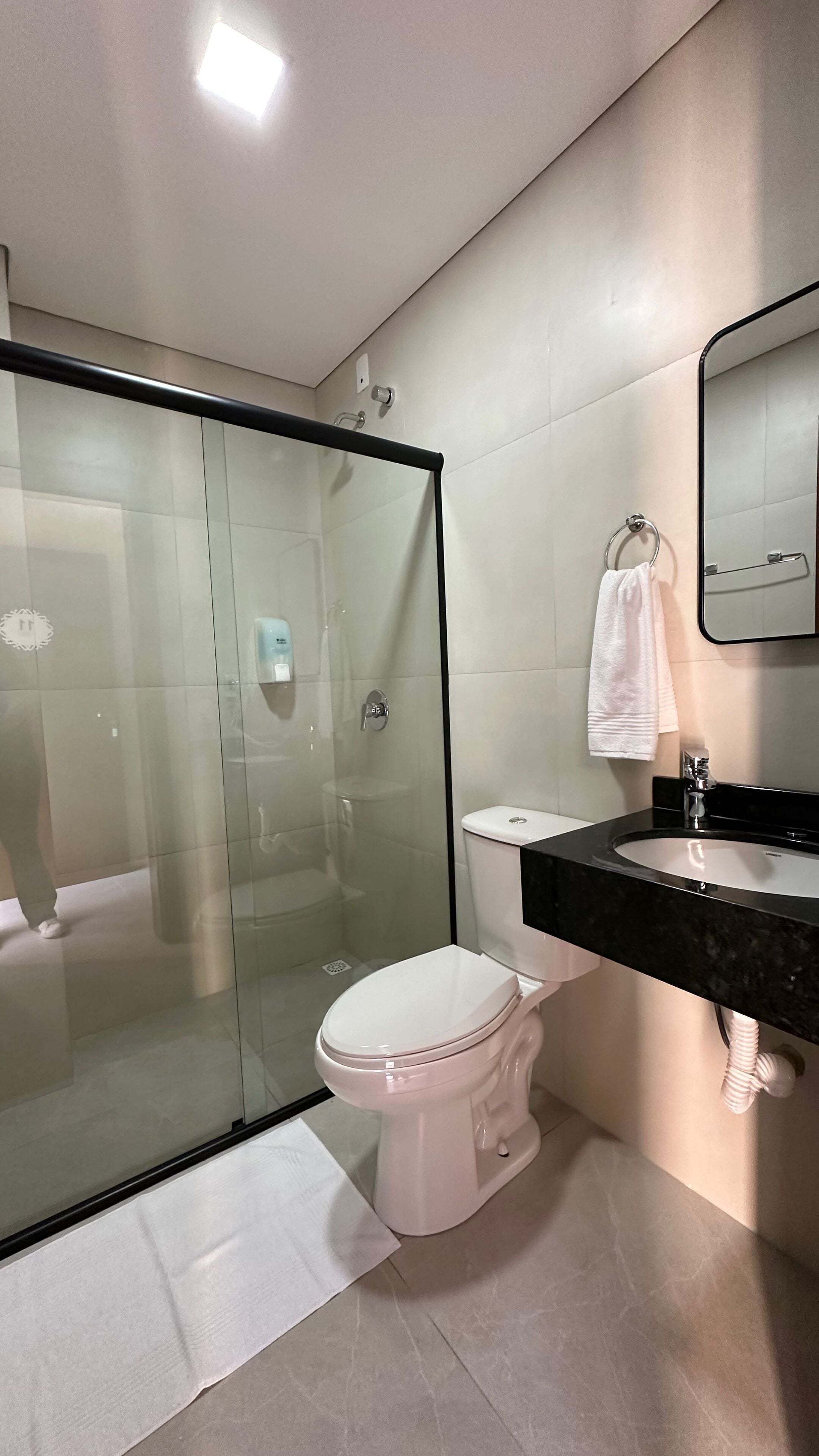 Une salle de bain moderne avec une douche à parois de verre, des toilettes blanches, un lavabo noir avec un miroir au-dessus, et une serviette accrochée au mur.