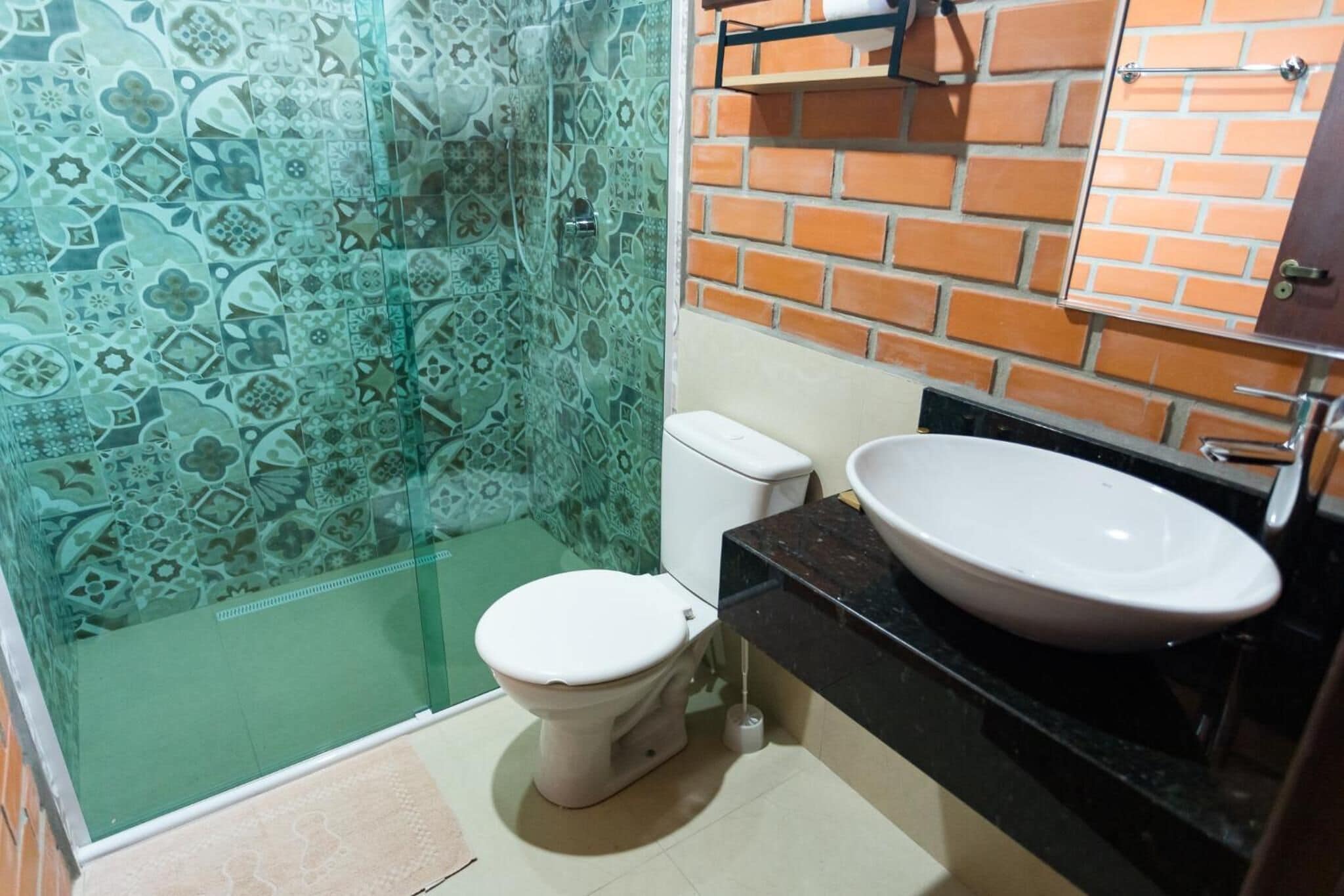 Un baño con cabina de ducha de vidrio, inodoro blanco, encimera negra y lavabo blanco.
