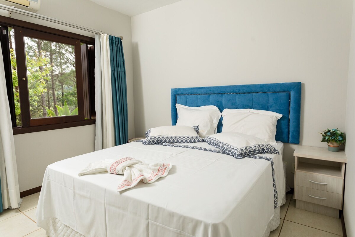 A neatly made bed with a blue headboard, white bedding, and a towel on the side.