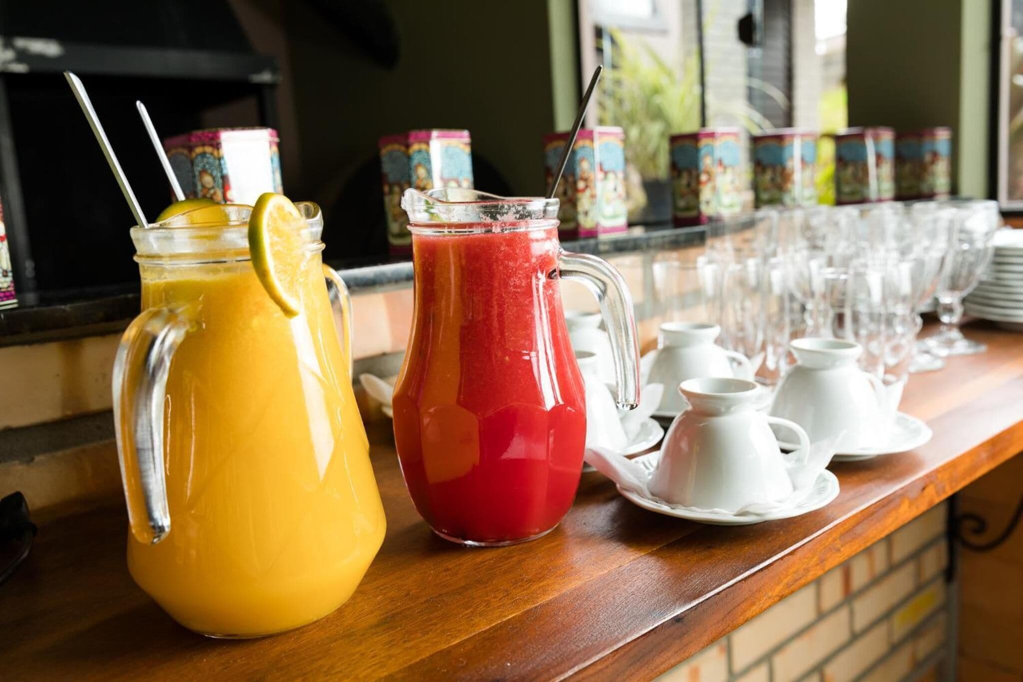 Una barra de desayuno con dos jarras de jugo y una selección de tazas y platillos de té blancos.