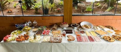 A buffet table with various food items and a view of a garden through a window.