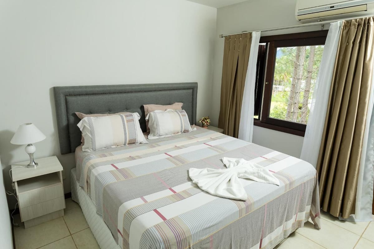A neatly made bed with a striped bedspread, a bedside lamp, and a window with curtains.