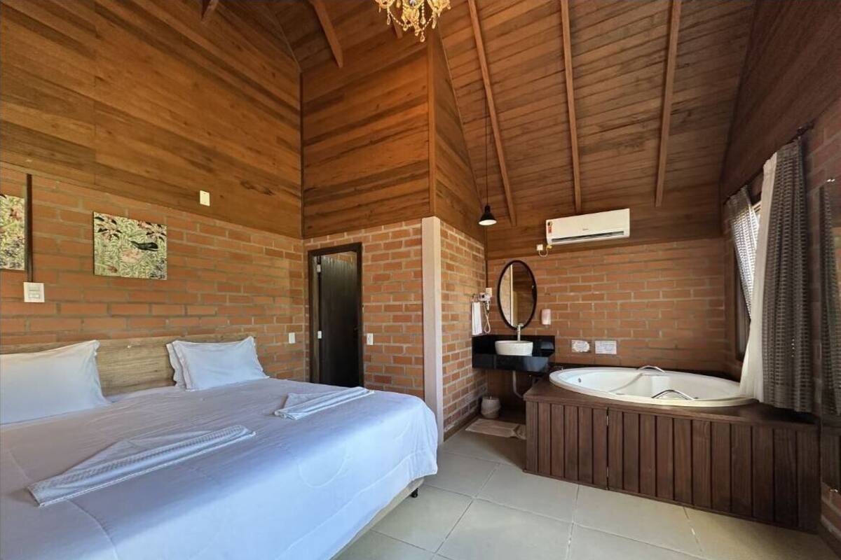 A room with a wooden ceiling, a large bed with white linens, a wooden bathtub, and a brick wall.