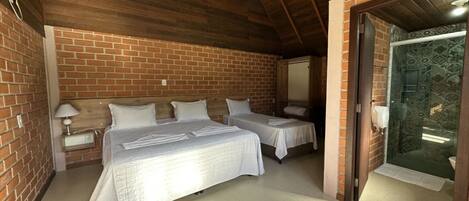 Una habitación con dos camas, una pared de ladrillo, techo de madera y una puerta de cristal que da a un baño.