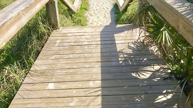 A wooden boardwalk leading to a beach with a clear view of the ocean.