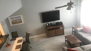 A modern living room with a flat-screen TV, a wooden coffee table, a sofa, and a dining area with chairs.